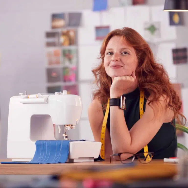 Small Business Marketing portrait of smiling female student or business owner working in fashion using sewing machine